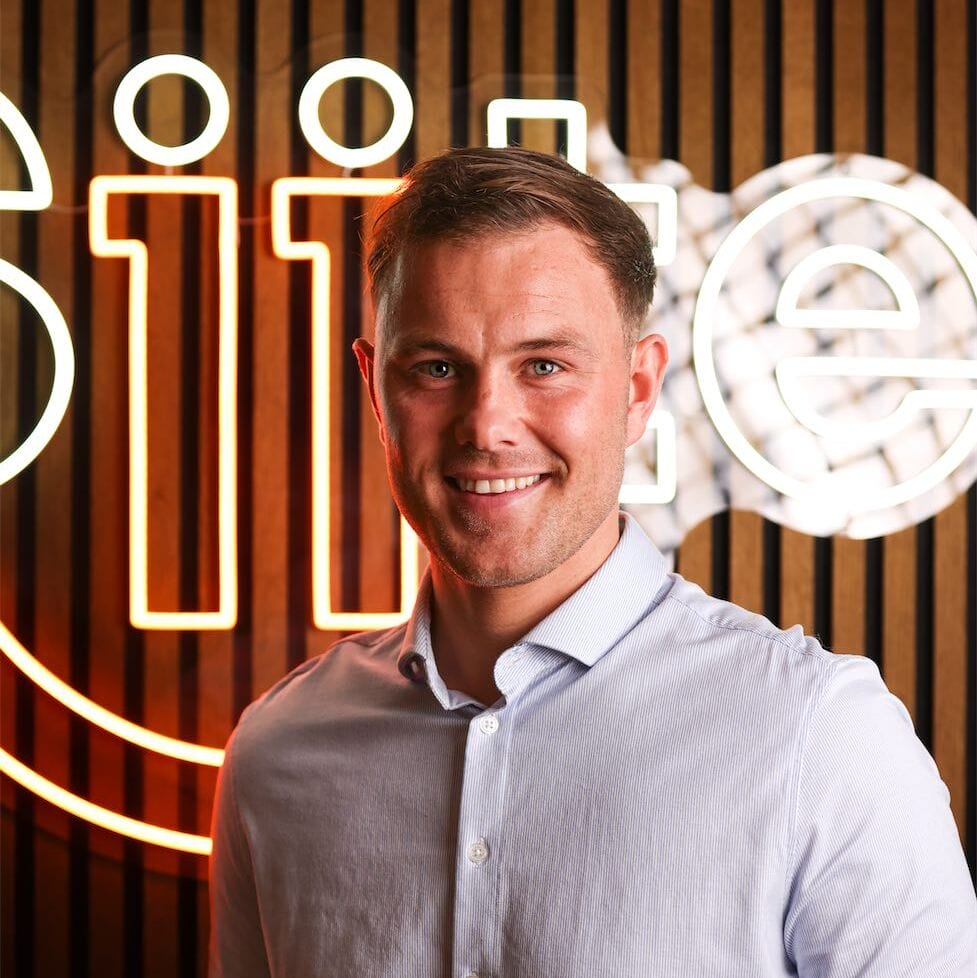 Smiling man in front of illuminated 'Google' sign.